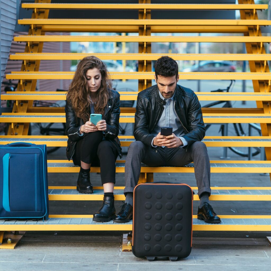 Couple with luggage, using mobile phone on steps, Florence, Italy