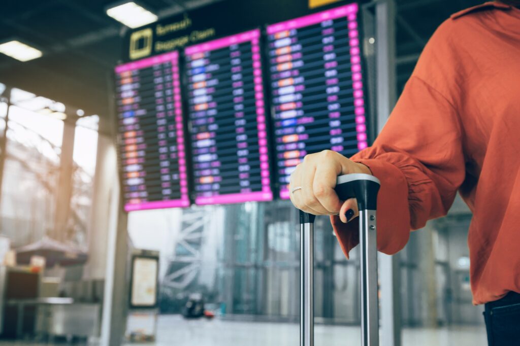 woman standing at the airport holding suitcase checking departure with the flight schedule